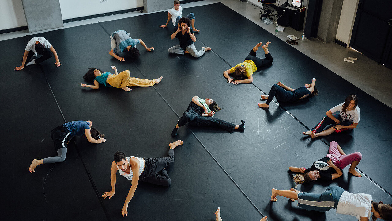 View from above on black dance floor. dancers spread out evenly, most of them in a lying position